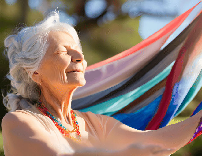 A serene, elderly woman gracefully practices yoga outdoors, her weathered face glowing with peace, framed by silver hair and draped in vibrant, flowing fabrics.
